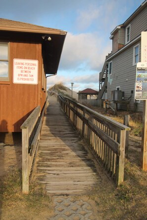 A wooden boardwalk leading to a building with a sign prohibiting leaving personal items on the beach between 8 PM and 7 AM.