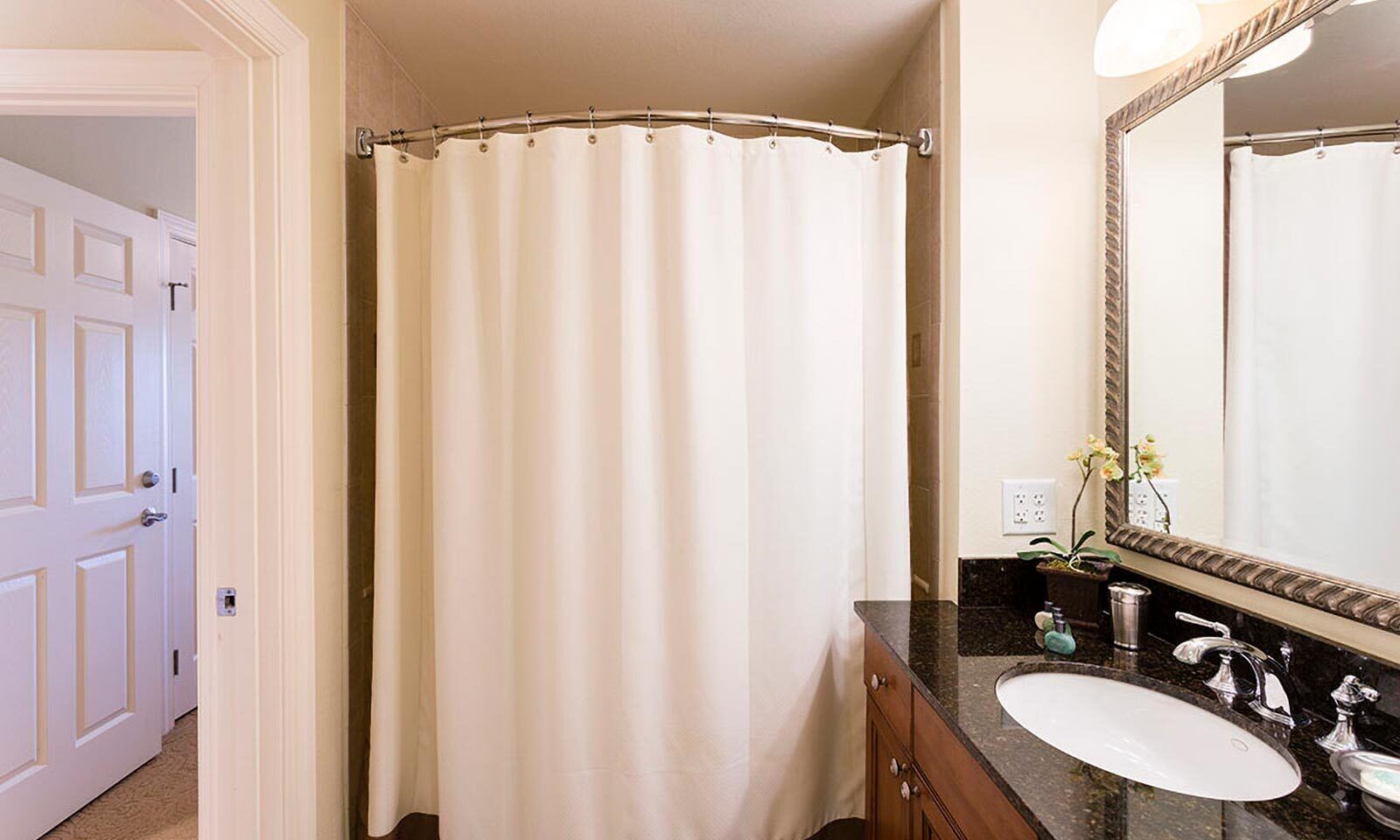 A bathroom with a shower curtain, a sink, a mirror, and a door.