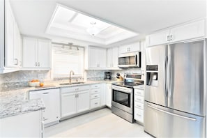 A modern kitchen with white cabinetry, stainless steel appliances, and a herringbone marble countertop.
