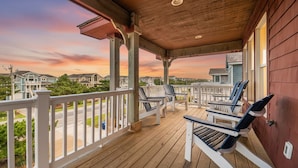Una terraza de madera con barandillas blancas y sillas Adirondack, con vista a una zona residencial.