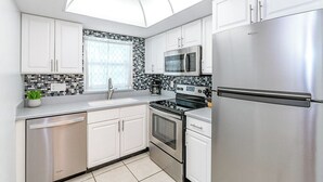 Una cocina moderna con armarios blancos, un refrigerador de acero inoxidable, un microondas, un horno y un lavavajillas.