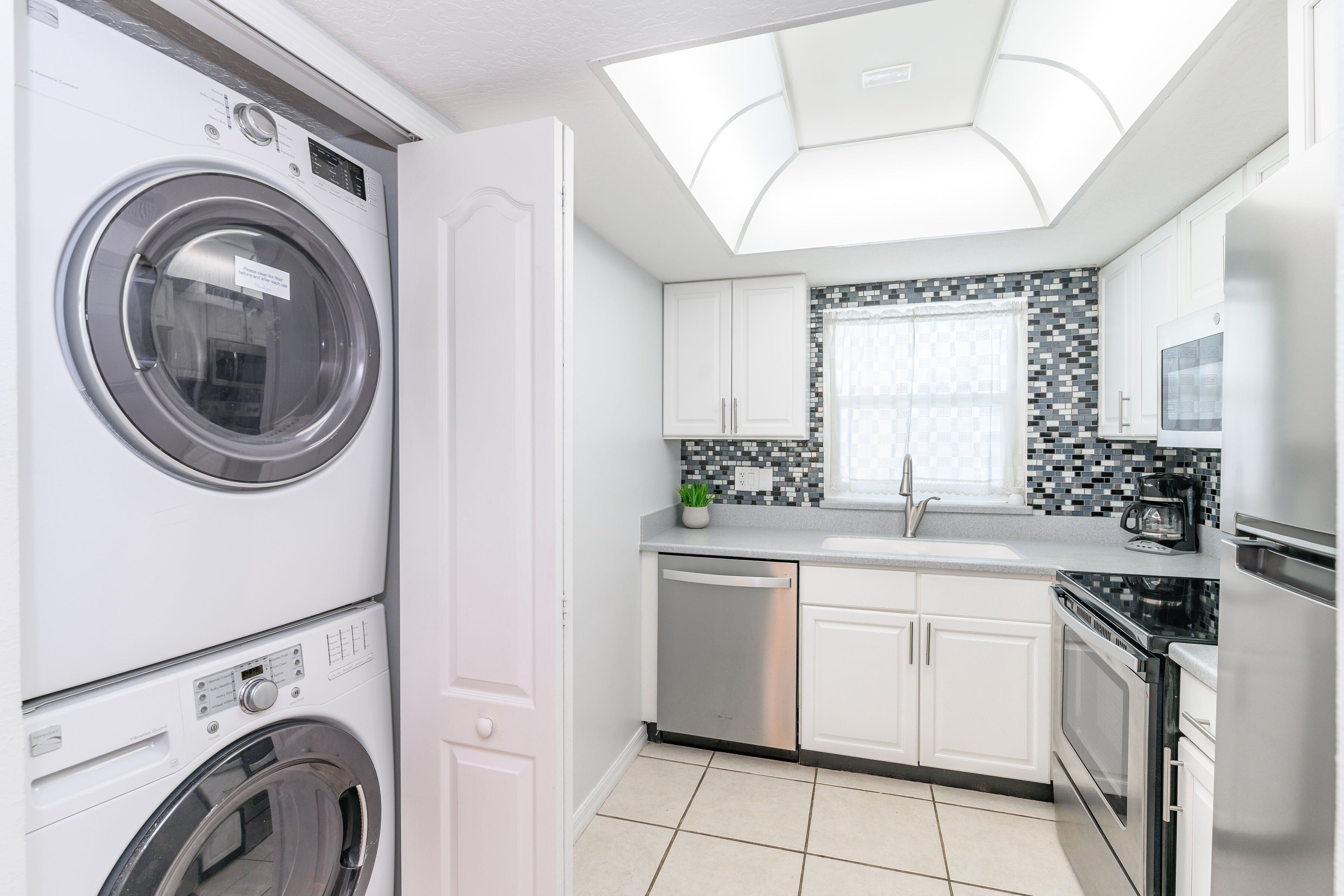 A modern kitchen with a built-in washer and dryer, white cabinets, a tiled backsplash, and a skylight.