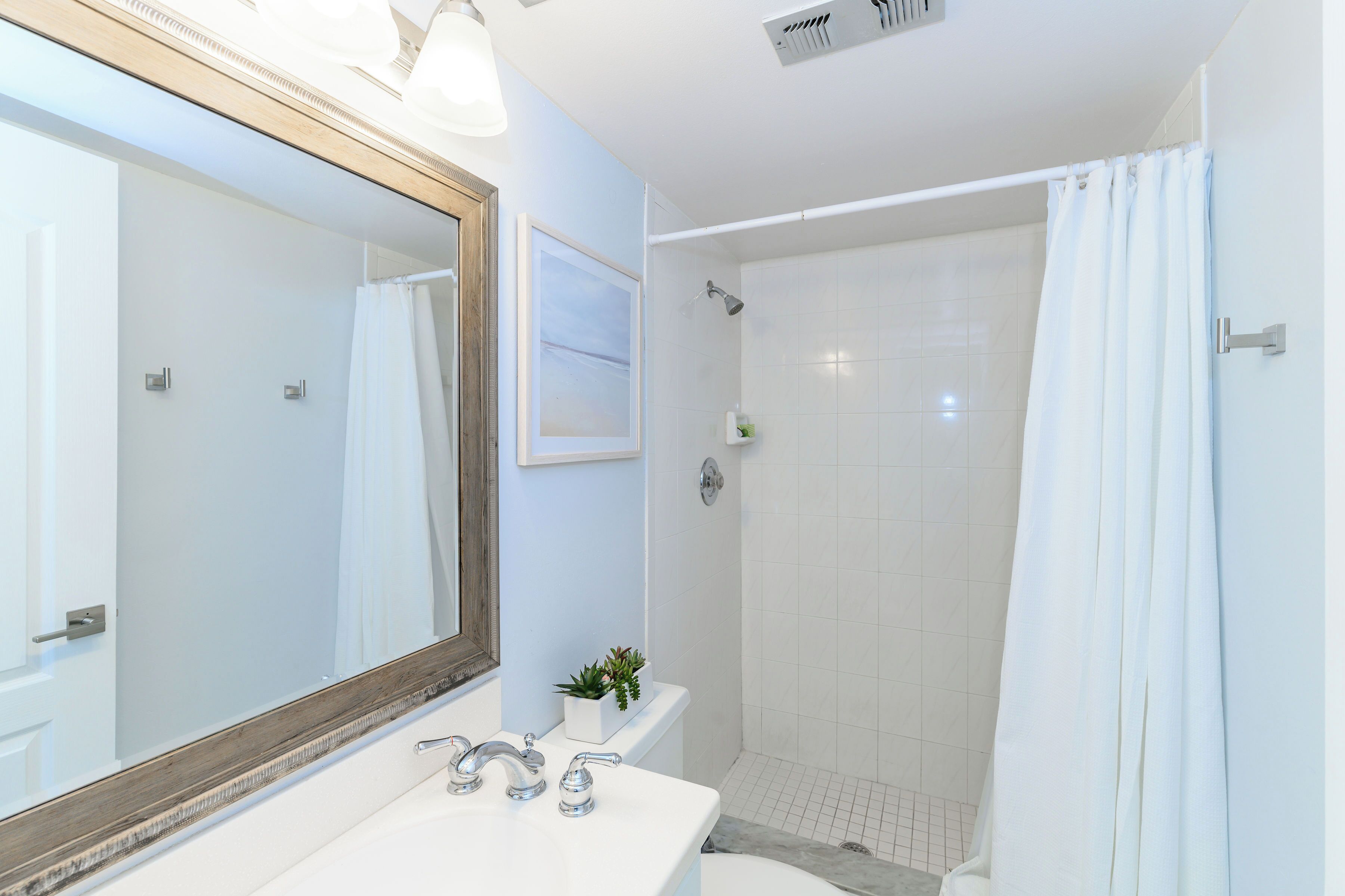 A modern bathroom with a large mirror, white sink, and shower area.