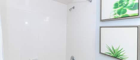 A bathroom with white tiles, a bathtub, a showerhead, and framed plant pictures on the wall.
