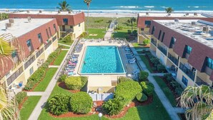 Un hotel con piscina central, vistas a la playa y un jardín bien cuidado.