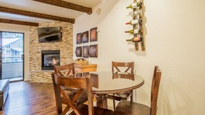 Un comedor con una mesa redonda y sillas de madera, una chimenea, un televisor montado en la pared y una estantería para vinos con botellas.
