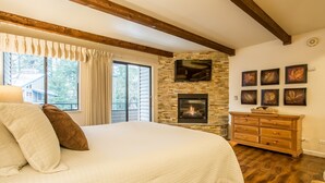 Un dormitorio con una cama grande, una chimenea de piedra, vigas de madera y una ventana con cortinas.