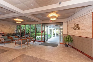 A lobby with a brick wall, wooden chairs, a large window, and a sign reading "Sea Watch". - Cute, cozy 2 bedroom oceanfront condo with free WiFi, a great ocean view, and awesome amenities including indoor/outdoor pools and a game room located uptown! (Ocean City)