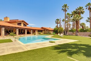 Une maison avec une piscine, une terrasse et une pelouse agrémentée de palmiers.