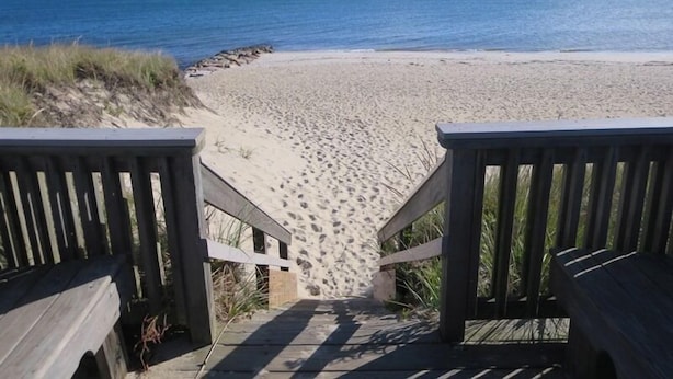 Pasarela de madera que conduce a una playa arenosa con huellas, con vista al océano.
