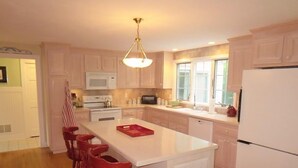 Una cocina moderna con una isla central, sillas de madera, un refrigerador blanco y una ventana que proporciona luz natural.