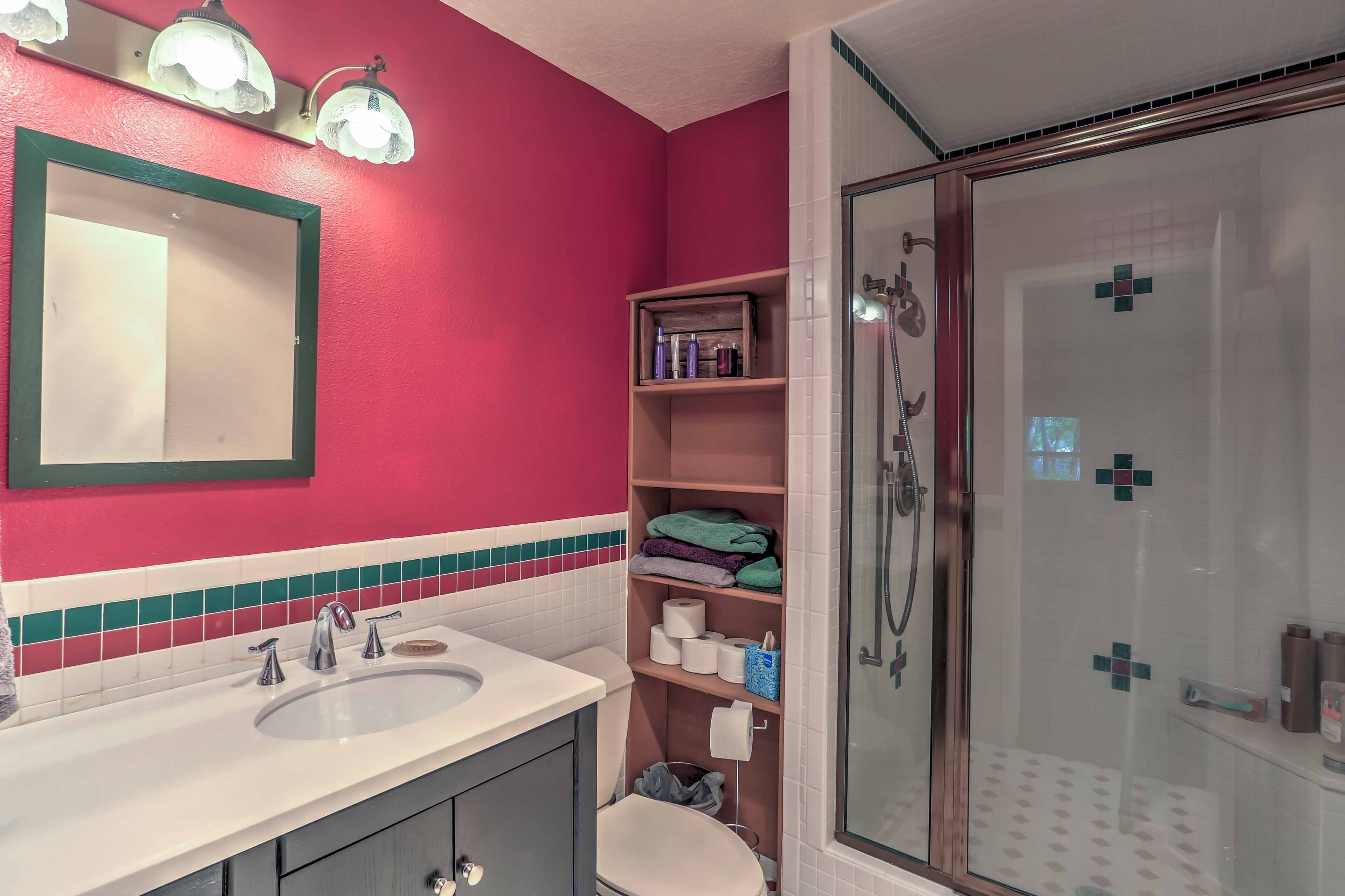 A bathroom with a pink wall, a white sink, a mirror, and a glass-enclosed shower.