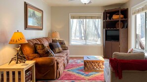 Un salon chaleureux avec un canapé en cuir marron, un tapis coloré, une table basse en bois et un téléviseur posé sur un meuble en bois.