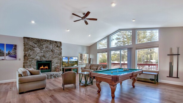A spacious living room with a pool table, a comfortable sofa, a stone wall, and a fireplace. - Blackfoot Family Estate (South Lake Tahoe)