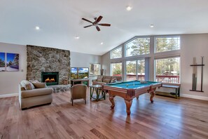 A spacious living room with a pool table, a comfortable sofa, a stone wall, and a fireplace. - Blackfoot Family Estate (South Lake Tahoe)
