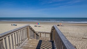 Una passerella in legno che conduce a una spiaggia con ombrelloni e persone che si rilassano.