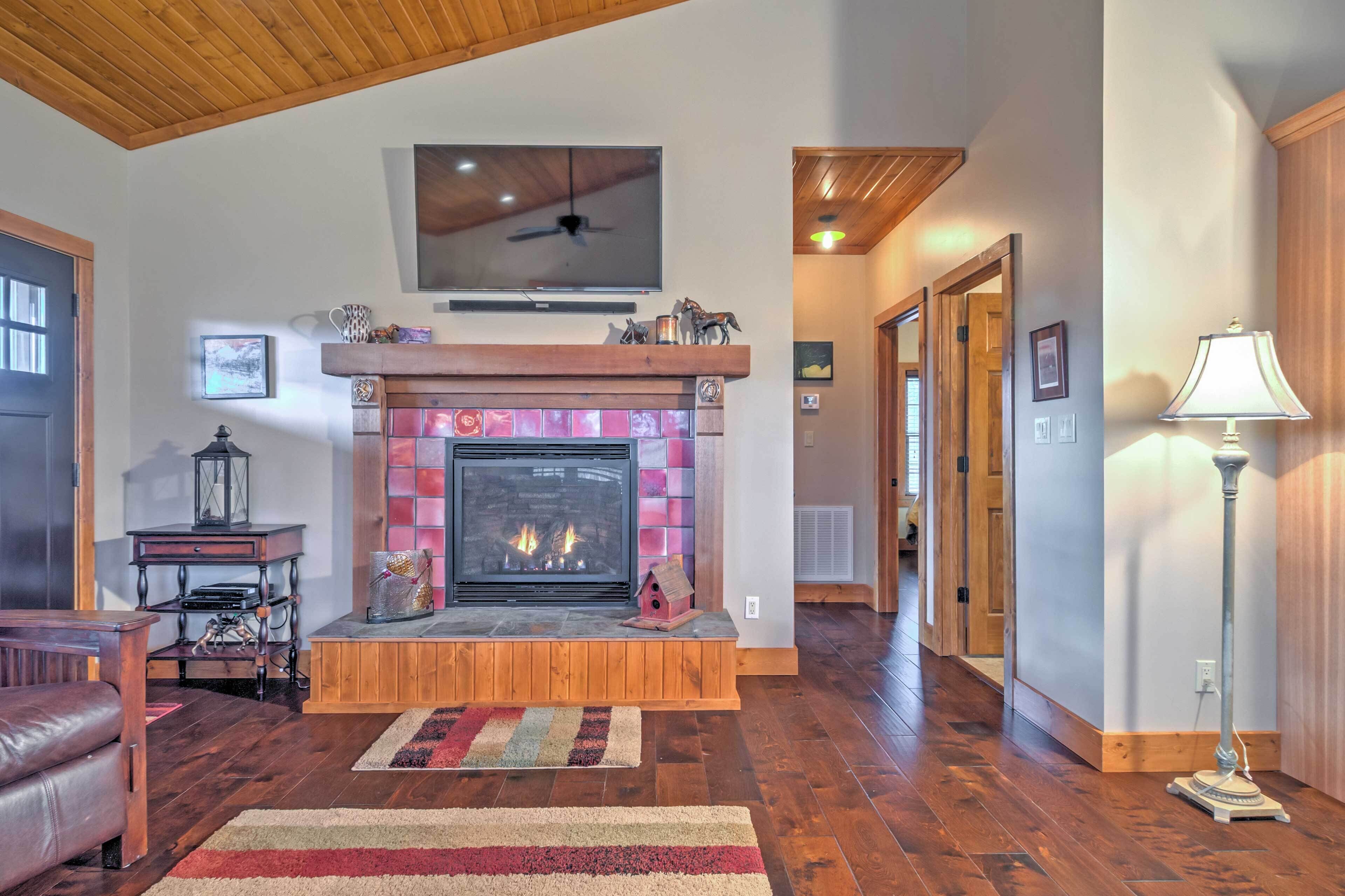 A cozy living room with a fireplace, wooden flooring, a leather couch, and a television mounted above the fireplace.