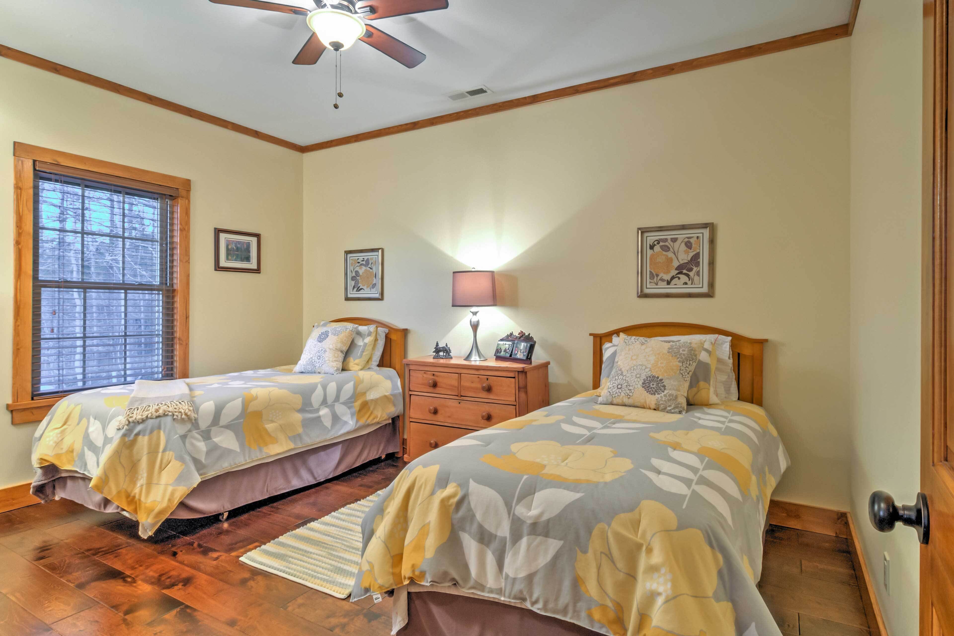 A bedroom with two beds, wooden flooring, a ceiling fan, and a window with blinds.
