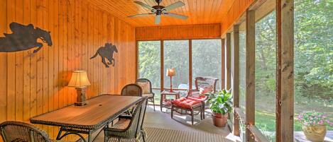 A wooden interior with a dining area, wicker furniture, and large windows.