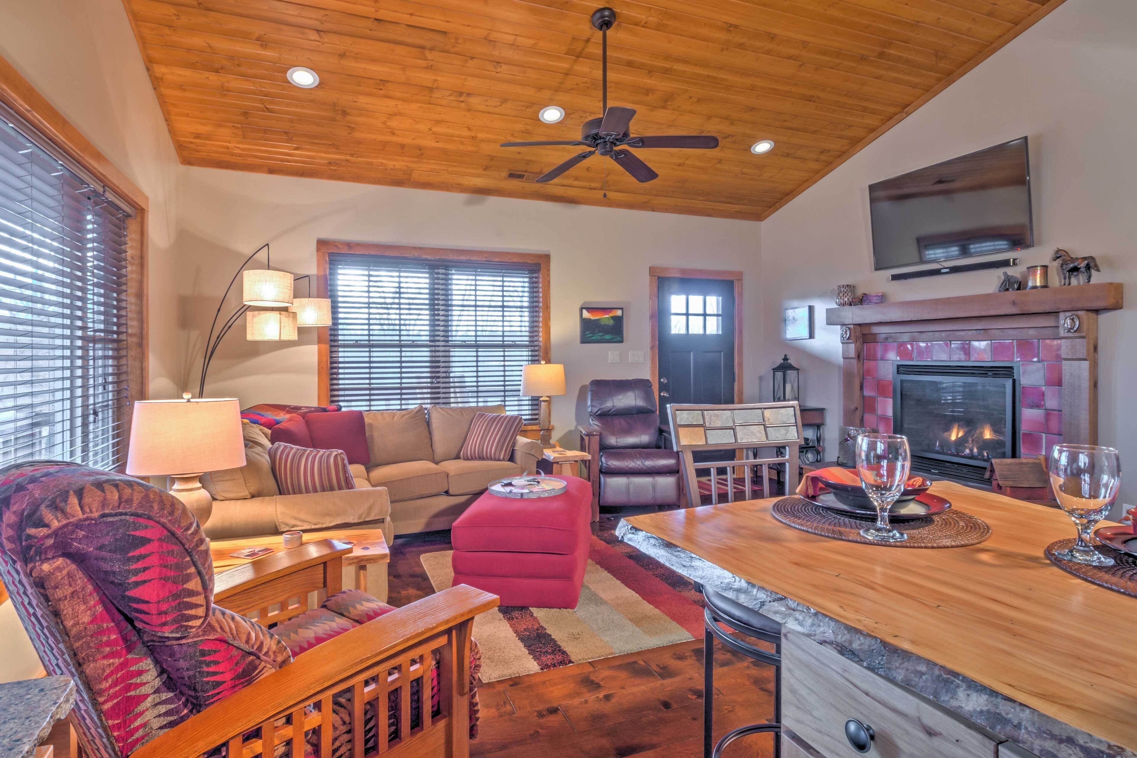 A cozy living room with a wooden ceiling, a fireplace, a television, and a dining area with a bar.