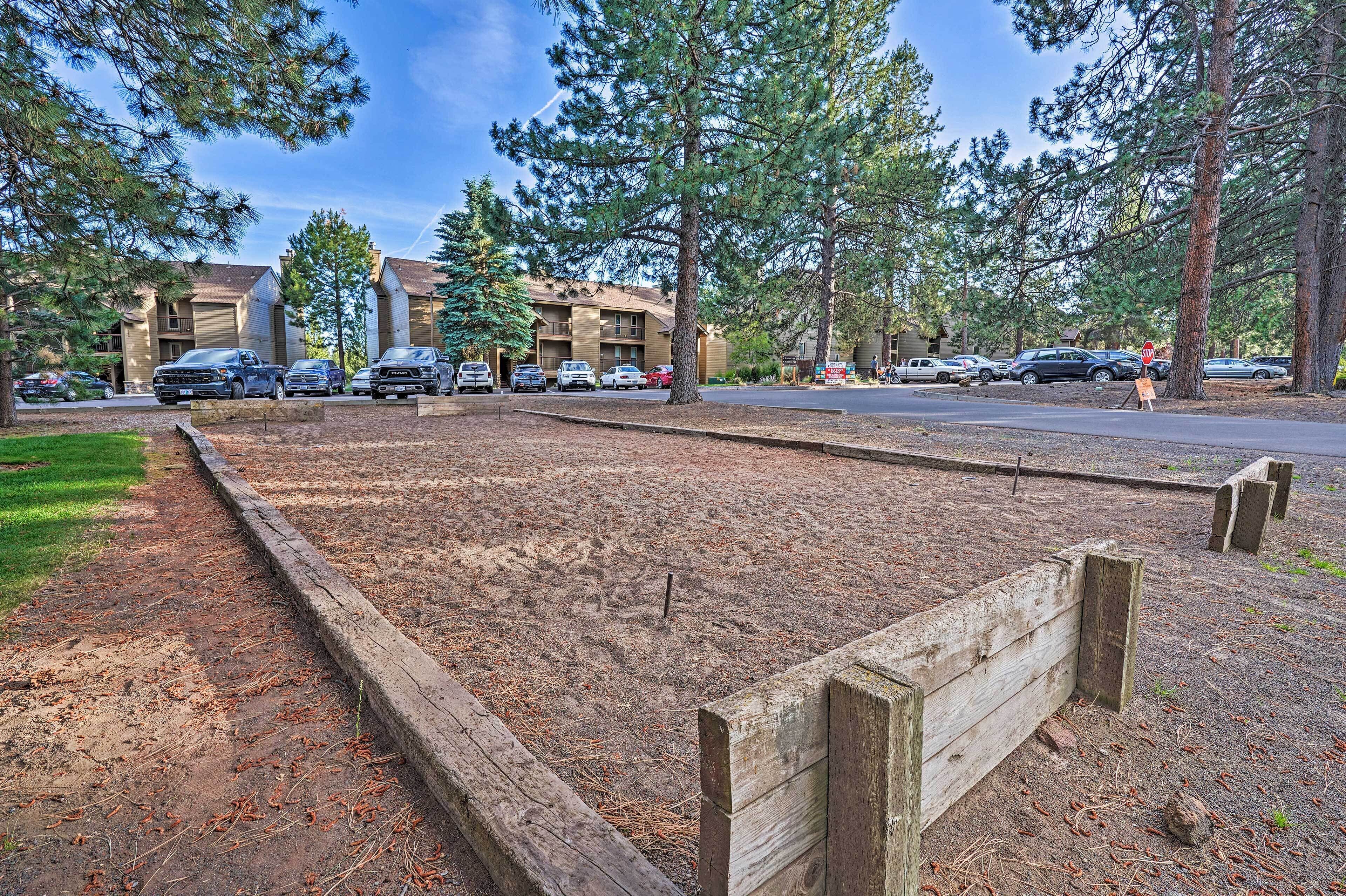 A parking lot with several cars, a wooden fence, and a building with multiple windows and a brown roof.