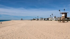 Una platja amb una torre de socorristes, palmeres i cases al fons.