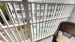 A balcony with white railings overlooking a swimming pool and a building with multiple balconies. - Myrtle Beach Villas 305B - 4 Bedroom Condo (Myrtle Beach)