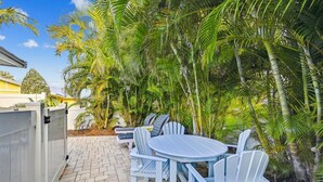 An outdoor patio with a round table and chairs, surrounded by palm trees. - Cozy Cottage for 4 located steps from the beach. Heated Pool in private Patio. (Holmes Beach)