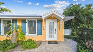 A two-story house with a yellow facade, blue shutters, and a white door. - Cozy Cottage for 4 located steps from the beach. Heated Pool in private Patio. (Holmes Beach)