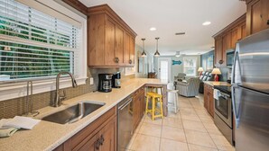 A modern kitchen with wooden cabinets, a stainless steel refrigerator, and a coffee maker. - Cozy Cottage for 4 located steps from the beach. Heated Pool in private Patio. (Holmes Beach)