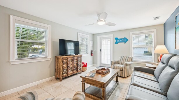A living room with a television, a wooden cabinet, a sofa, and a striped armchair. - Cozy Cottage for 4 located steps from the beach. Heated Pool in private Patio. (Holmes Beach)