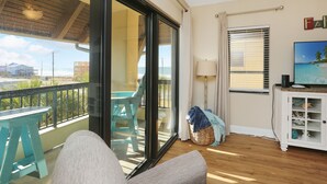 A balcony with a table and chairs, a sliding glass door, a TV on a cabinet, and a view of the beach. - Pool, Hot Tub, Elevator, Beach Views- Club at Mexico Beach 2D (Mexico Beach)