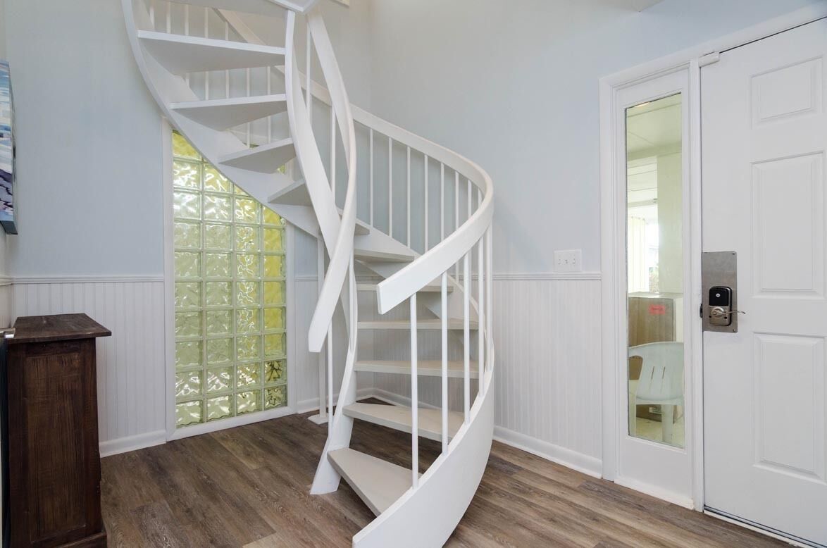Gradi d'espiral blancs en una habitació amb terra de fusta i una porta blanca amb un panell de vidre.