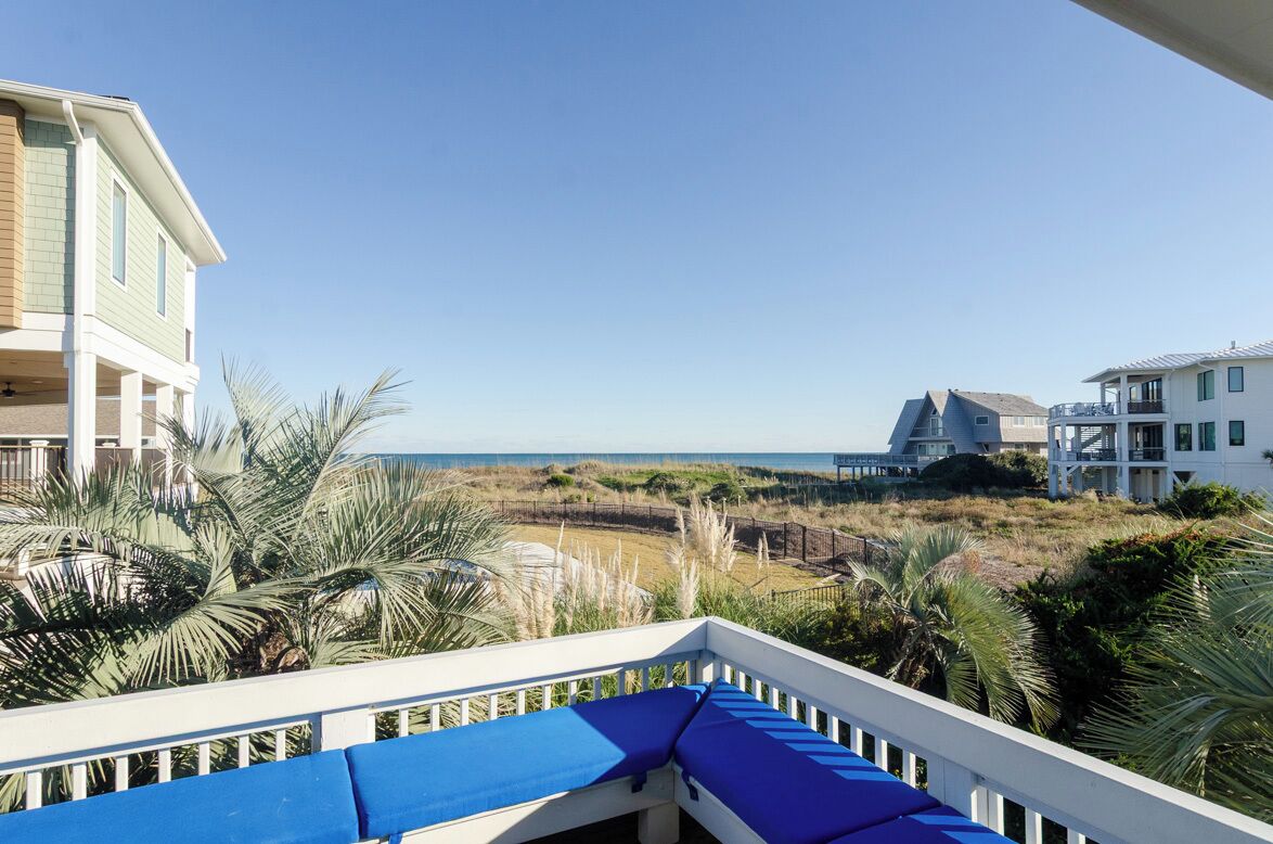 A balcony with a view of the beach and ocean, surrounded by palm trees and other vegetation.
