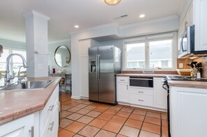 A modern kitchen with white cabinetry, a stainless steel refrigerator, a sink, and a window providing natural light.