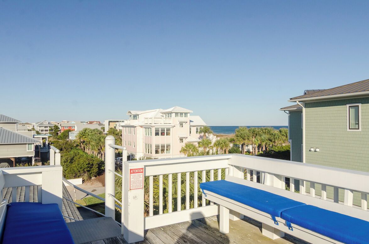 A balcony with a blue cushion, a white railing, and a view of the beach and ocean.