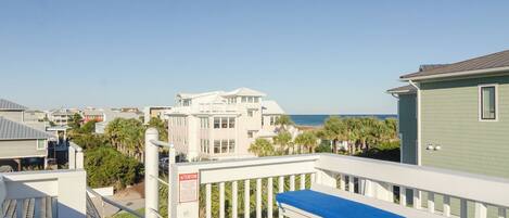 A balcony with a blue cushion, a white railing, and a view of the beach and ocean.