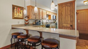 Une cuisine avec des meubles en bois, un plan de travail en granit et un coin bar avec des tabourets.