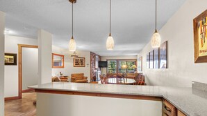 Une cuisine spacieuse dotée d’un grand îlot central, de luminaires suspendus et d’un coin repas offrant une vue sur l’extérieur.