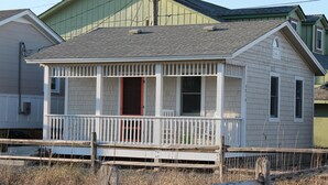 A small, single-story house with a porch and a red door. - Kemp & Olive Cottage: Tiny Cottage for Two Guests and Pups! (Nags Head)