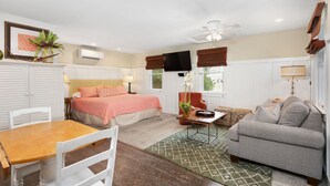 A room with a bed, a sofa, a dining table, and a TV. - Kemp & Olive Cottage: Tiny Cottage for Two Guests and Pups! (Nags Head)