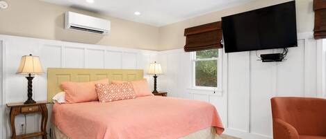 A bedroom with a bed, two bedside tables with lamps, a television mounted on the wall, and a window with blinds.