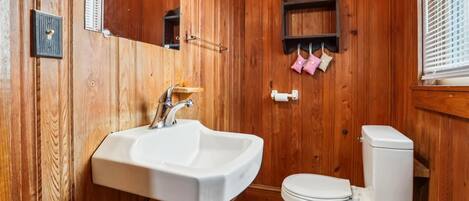 Un bagno con arredamento in legno, un lavandino bianco, un water e uno specchio.