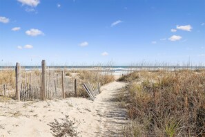 Un sendero arenoso que lleva a una playa, con una valla de madera a la izquierda.