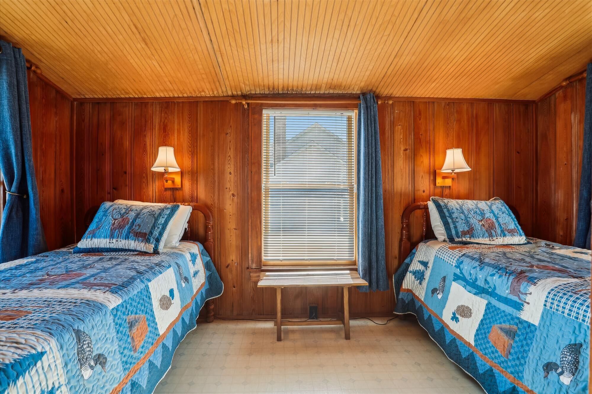 Een kamer met twee bedden, houten wanden, een raam met zonwering en wandlampen.