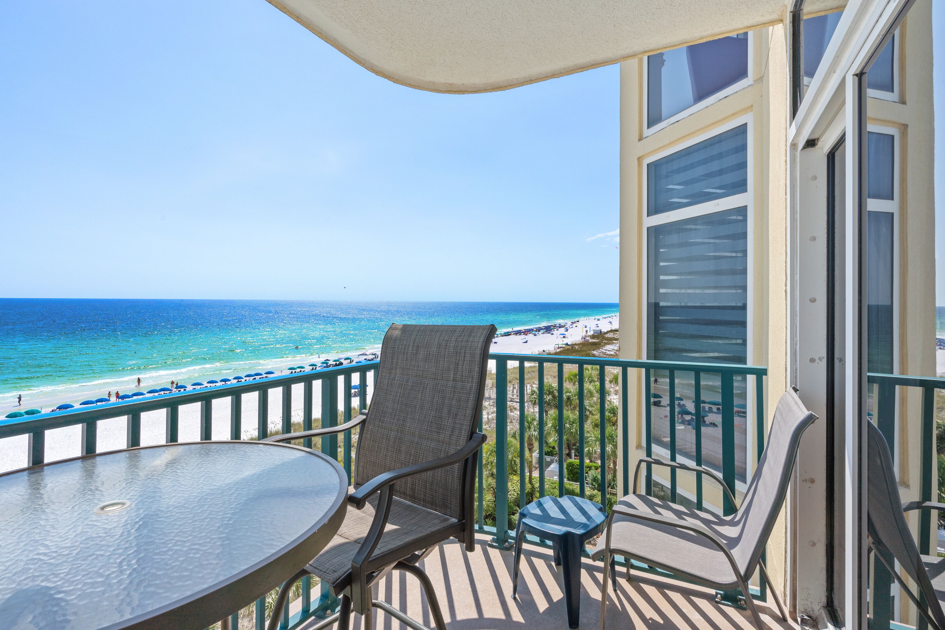 A balcony with a glass table and chairs overlooking a beach.