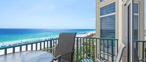 A balcony with a glass table and chairs overlooking a beach.