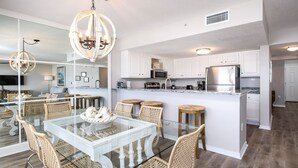 A modern kitchen with white cabinets, stainless steel appliances, and a glass dining table with wicker chairs.