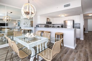 Une cuisine moderne avec des meubles blancs, un réfrigérateur en acier inoxydable et une table à manger en verre, assortie de chaises en osier.