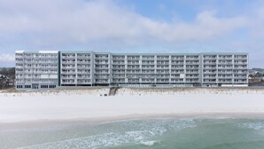 A multi-story hotel with balconies, located adjacent to a sandy beach.
